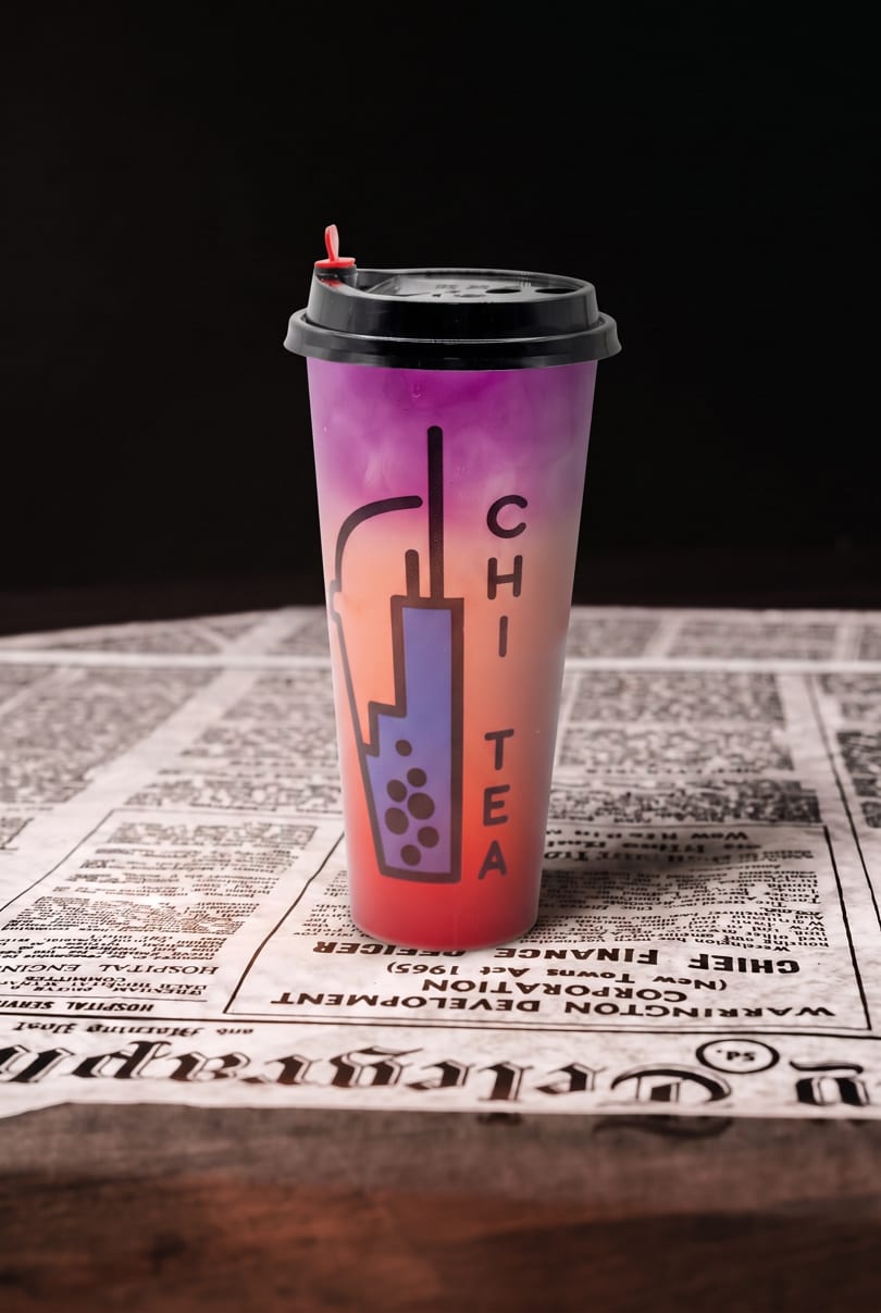 Gradient purple and orange bubble tea cup with 'CHI TEA' logo on a newspaper.