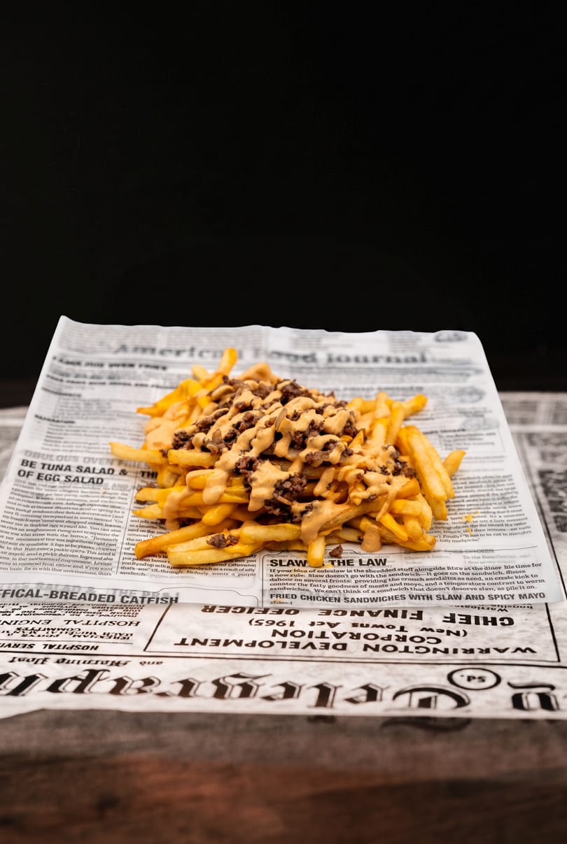 Loaded french fries with cheese sauce and ground beef, served on newspaper print.