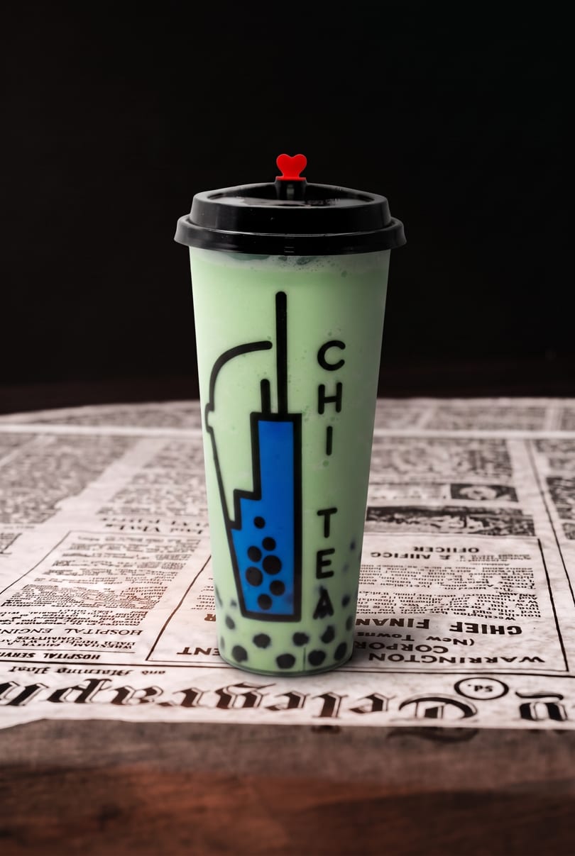 Green bubble tea with a 'CHI TEA' logo and red heart stopper on a newspaper.