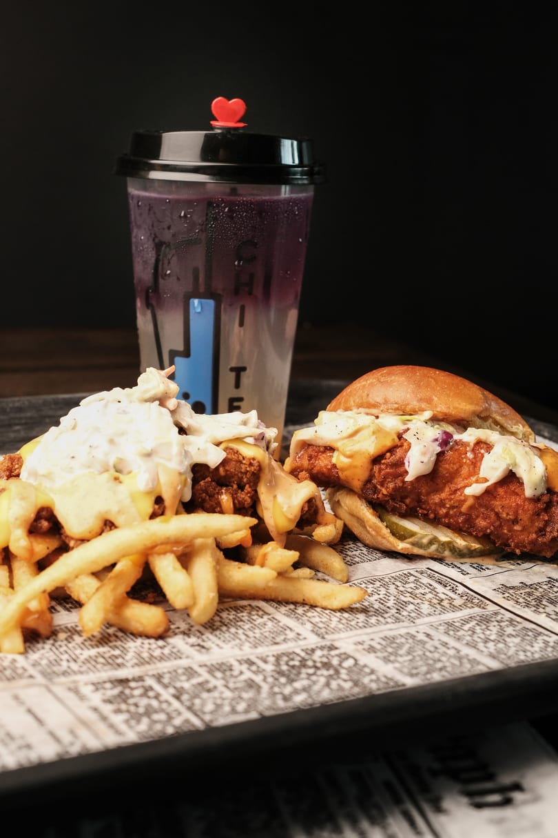 A fried chicken sandwich, loaded fries, and a purple drink on a tray with newspaper lining.