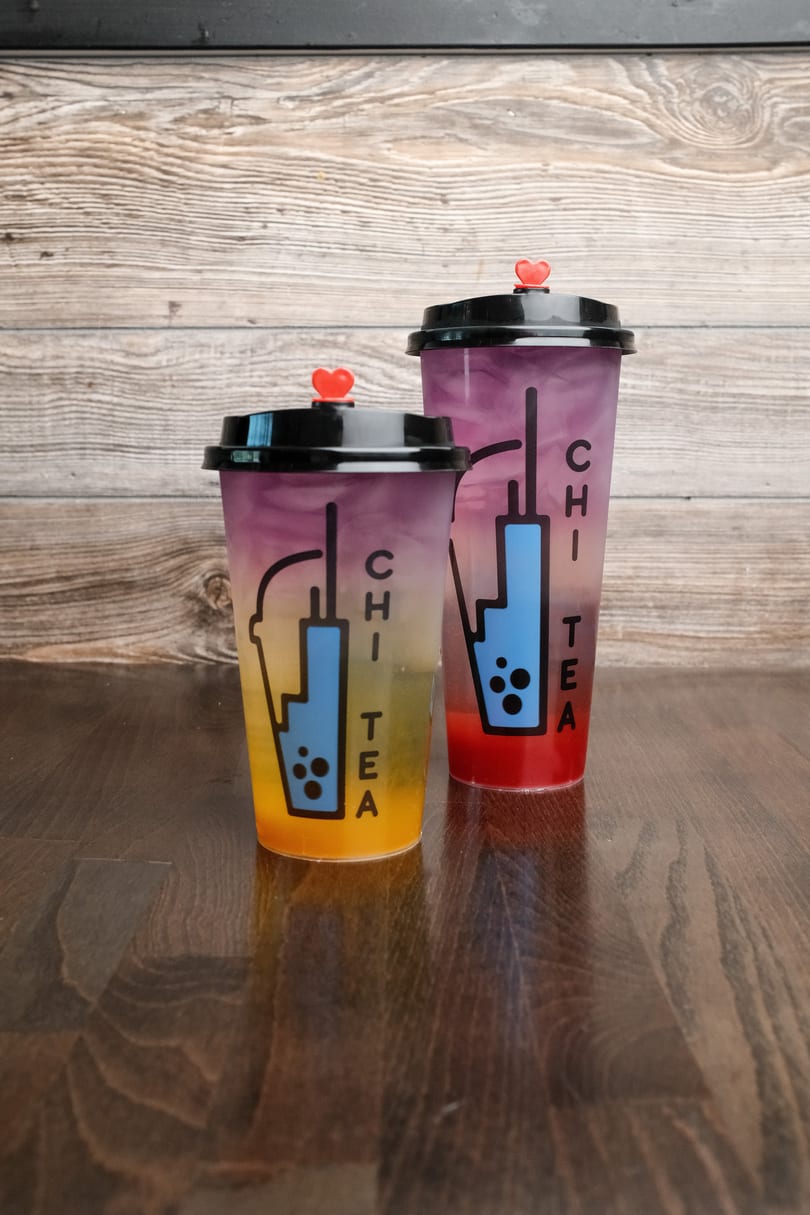 Two colorful Chi Tea drinks with heart-shaped stoppers on a wooden table.