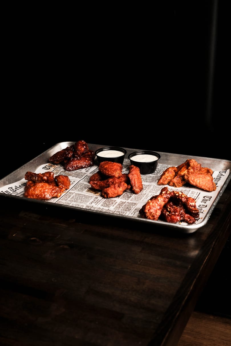 A metal tray with five piles of chicken wings and two small cups of dipping sauce.
