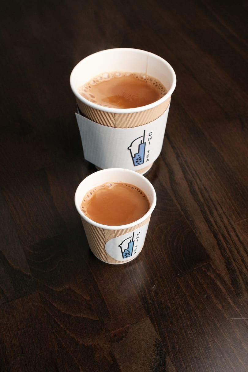 Two cups of Chi Tea, one large and one small, on a dark wooden table.